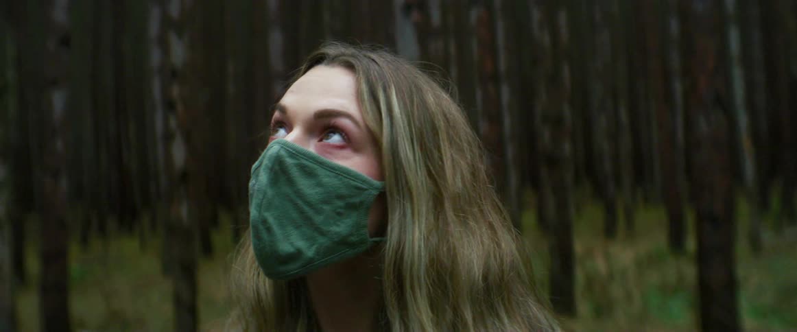 Woman with a green mask looks around in the woods