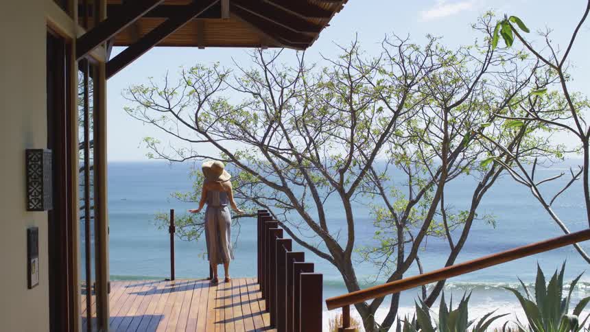 A woman stands on a patio outside a building and looks out at the water