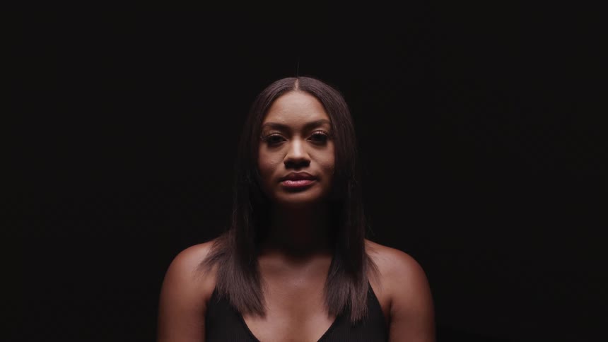 Woman with straight hair raises her head to look at the camera on the dark background