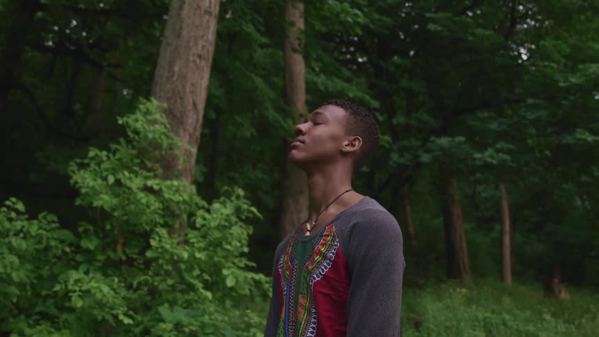 Young man standing near a forest looking up at the sky