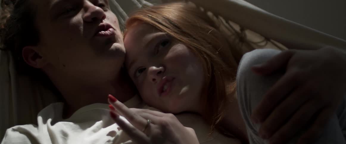 Young couple talking while resting on a hammock inside a dimly lit room