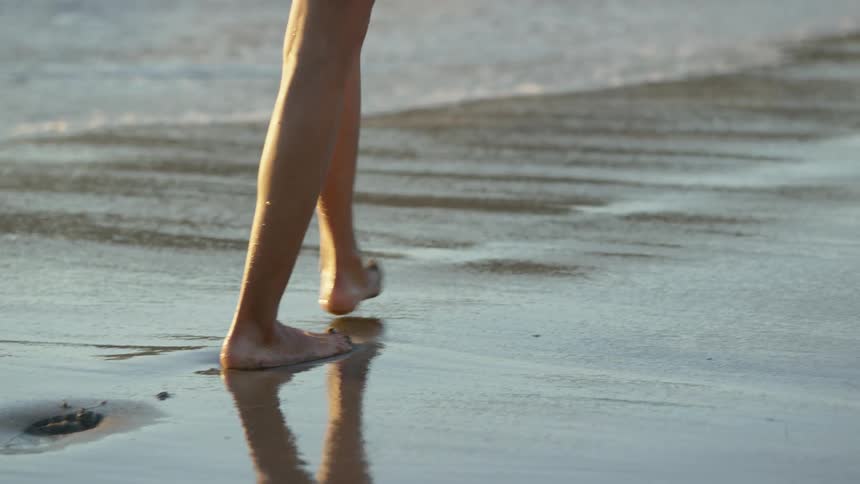Person walks along beach as surf rolls in and covers their feet
