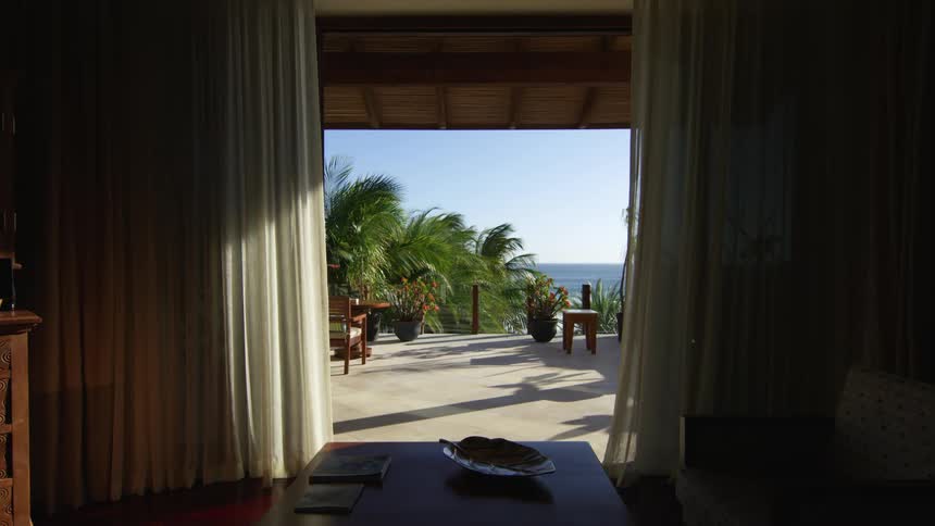 A view out of a hotel room at trees and the ocean