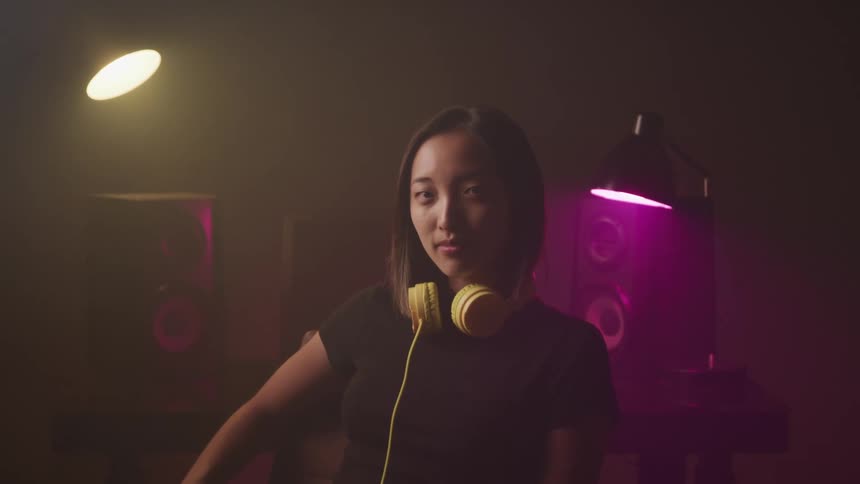 Female dj wearing yellow earphones on her neck looks at the camera