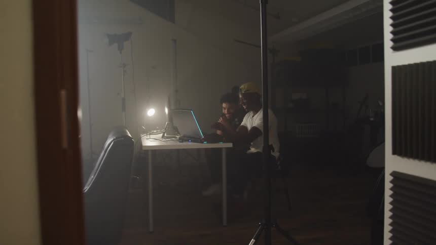 Two men sit at table smiling while viewing laptop surrounded by photography equipment
