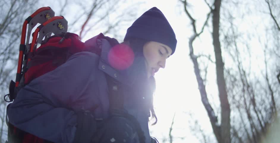A young woman in cold weather clothing hikes through a woodland during the day