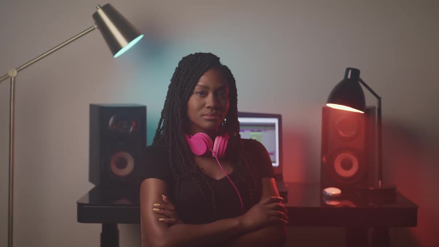 A woman standing and crossing her arms with headphones and speakers in the background