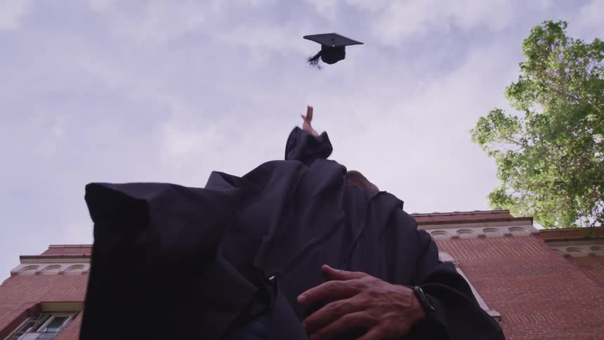 A male college student throwing a graduation cap into the air at graduation