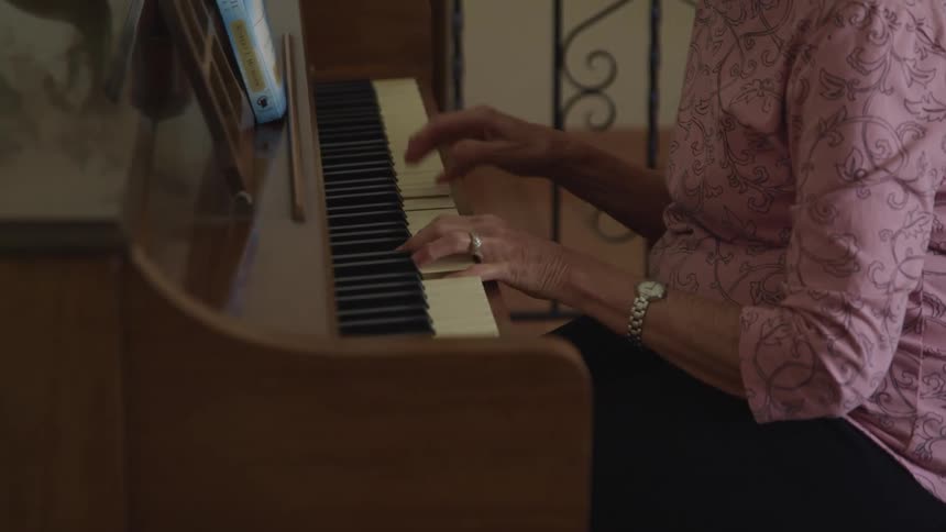 A woman sitting in a room playing a piano with a wall in the background