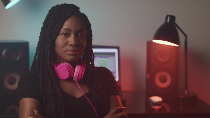 A woman with headphones with a lamp a table and a laptop in the background