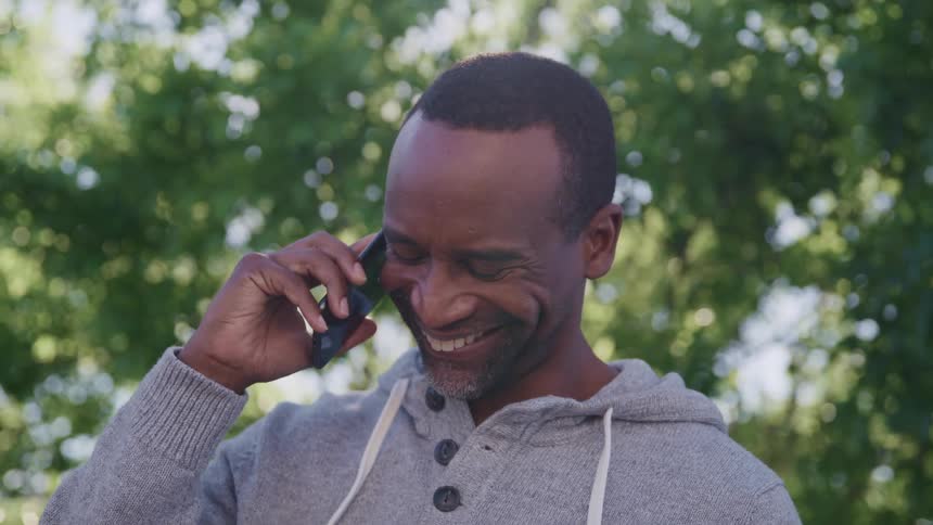 A man talking on a smart phone with trees the sky and clouds in the background