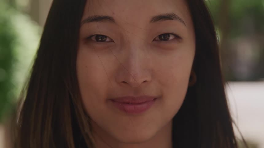 An asian woman smiles softly as the wind blows her hair