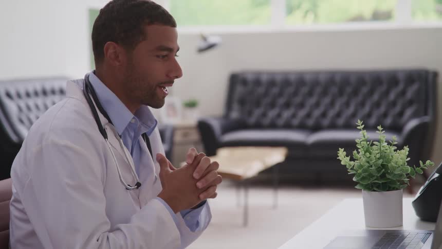 A doctor with a lab coat and a stethoscope in a room with a couch and a table in the background