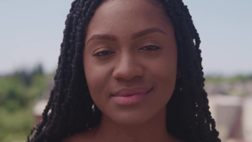 A black woman smiles softly while outside on a sunny day
