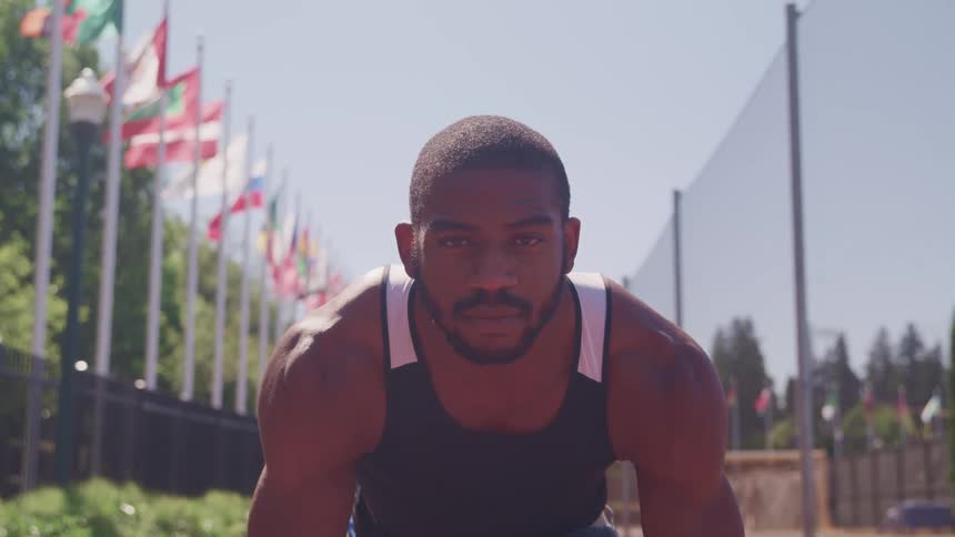 A muscular male athlete on an outdoor racing track on a summer day