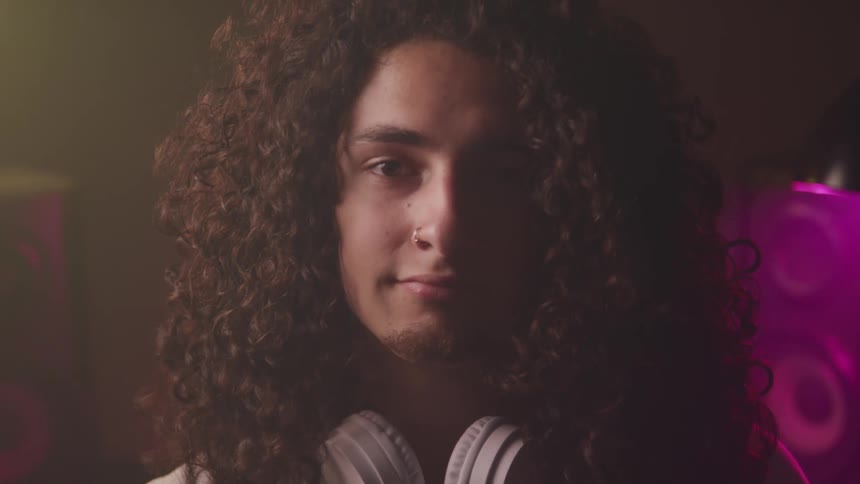Young man with long curly hair wearing headphones around his neck looks up to the camera