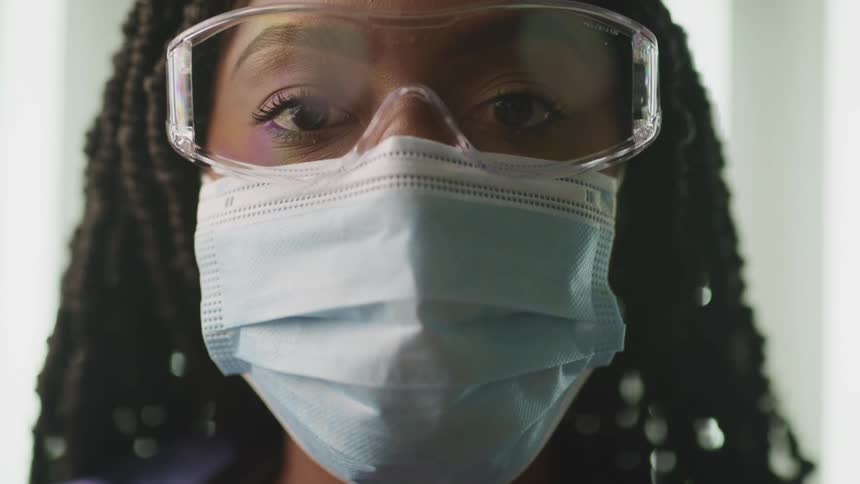 A nurse in personal protective equipment raises her head to gaze into the camera