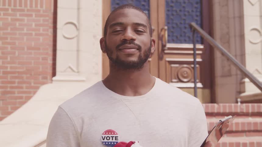 Young man with a vote pin on his shirt looking at the camera