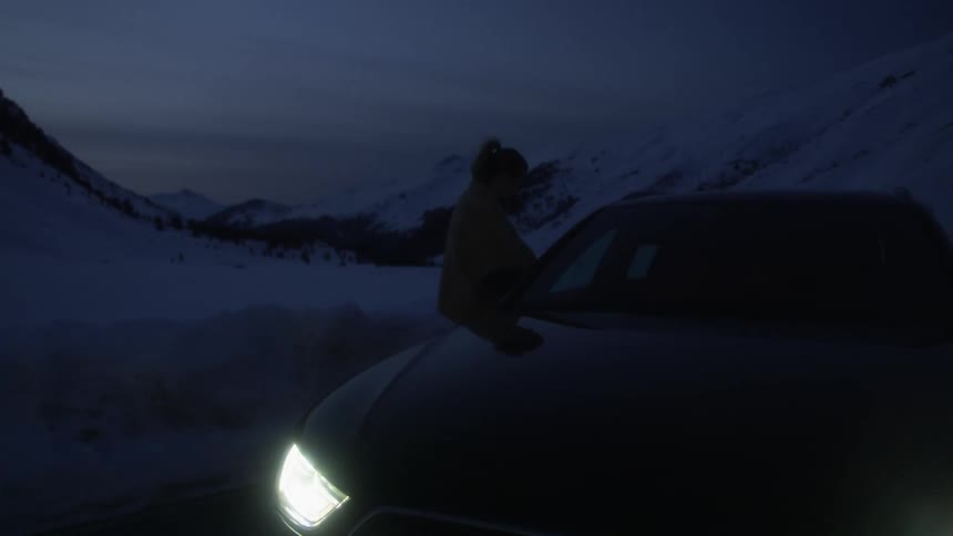 Woman boarding a car with headlights on parked on the snow covered mountain road