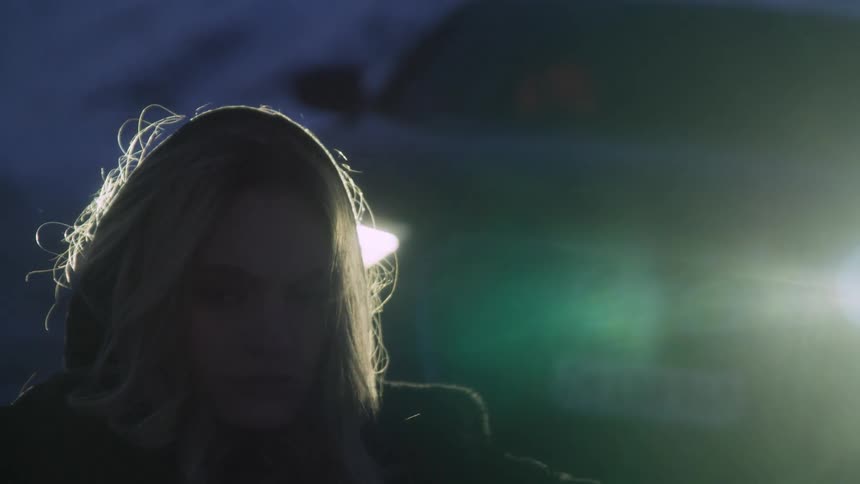 Silhouette of a woman in front of the headlights of a car parked in the mountains at winter