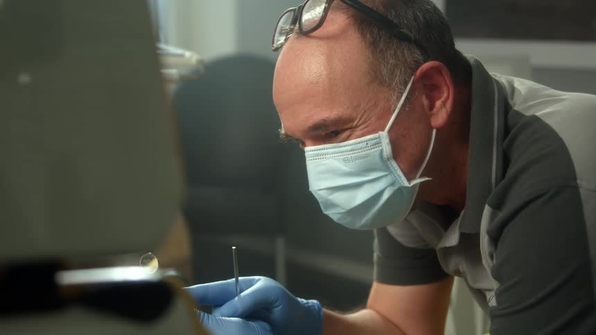 A dentist with gloves glasses and a mirror sitting in an office