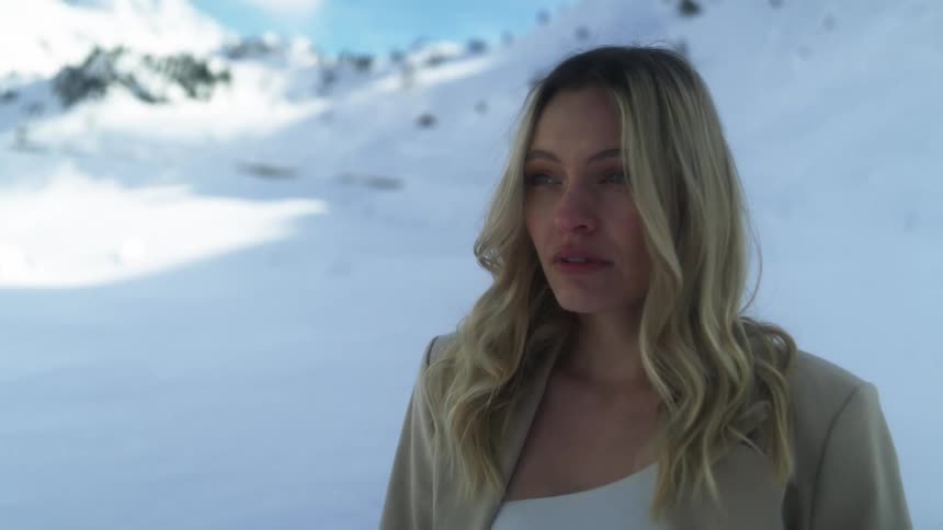 Young blonde woman standing on the snow covered slope of a mountain