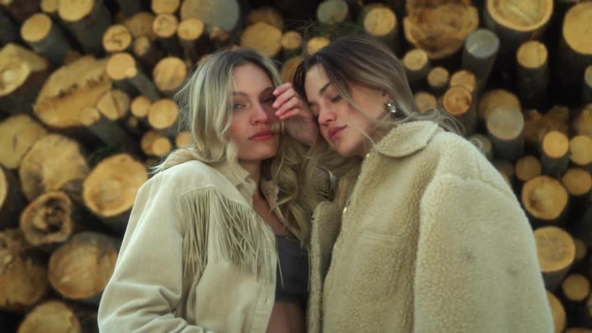 Two young models wearing coats in front of a pile of logs