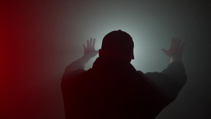 Man with arms raised towards a white light inside a room filled with smoke