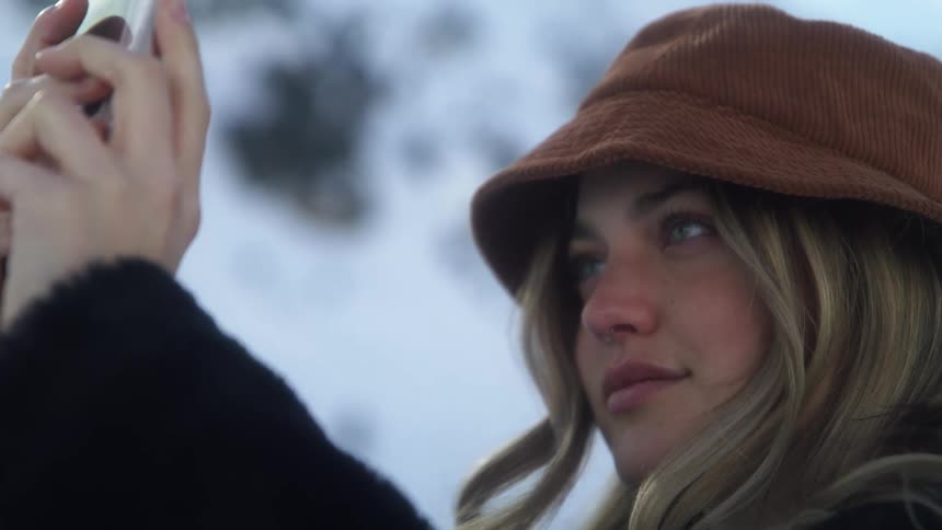 Blonde woman with brown hat takes pictures with a smartphone