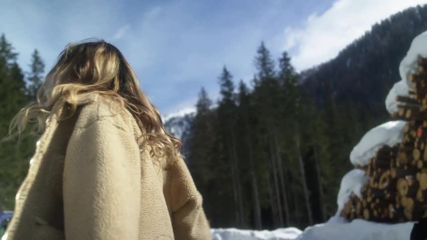 A woman jumps and twirls with joy near trees snow and mountain