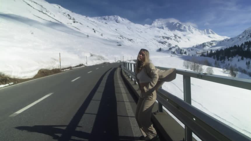 A teenage girl sitting on a railing on the side of a road jumps down on to the road