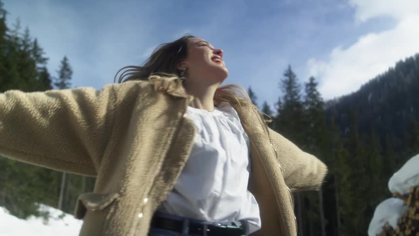 Happy woman spinning near a snow covered pile of lumber in the mountains