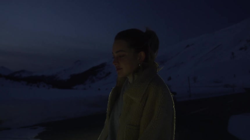 A woman with a jacket with a mountain range the sky and clouds in the background