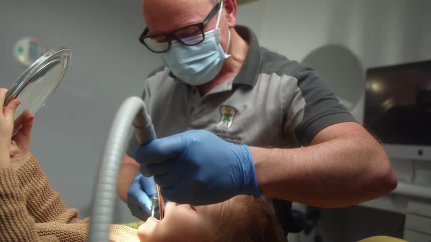 A dentist with a mask and glasses working on a boys mouth with tools