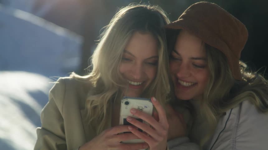 Two female friends smiling and laughing looking at a phone screen in the snow