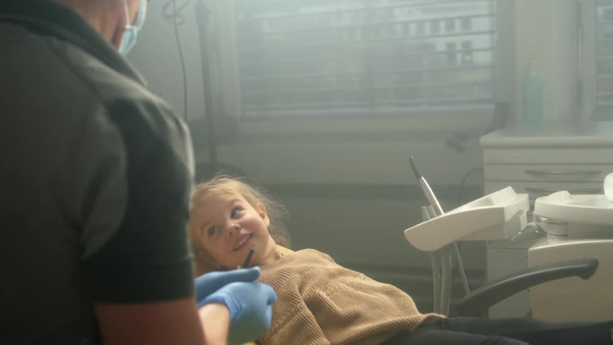 Smiling girl reclines in dentist chair next to dentist