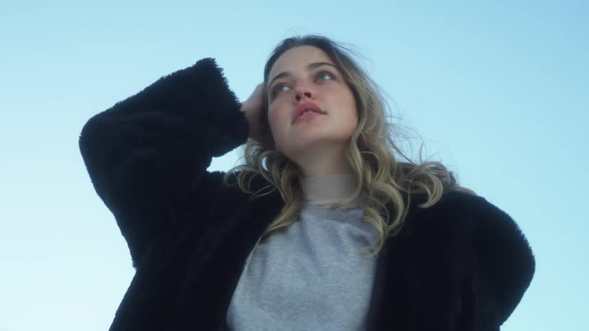 Young blonde woman wearing a black coat modeling looking at the camera