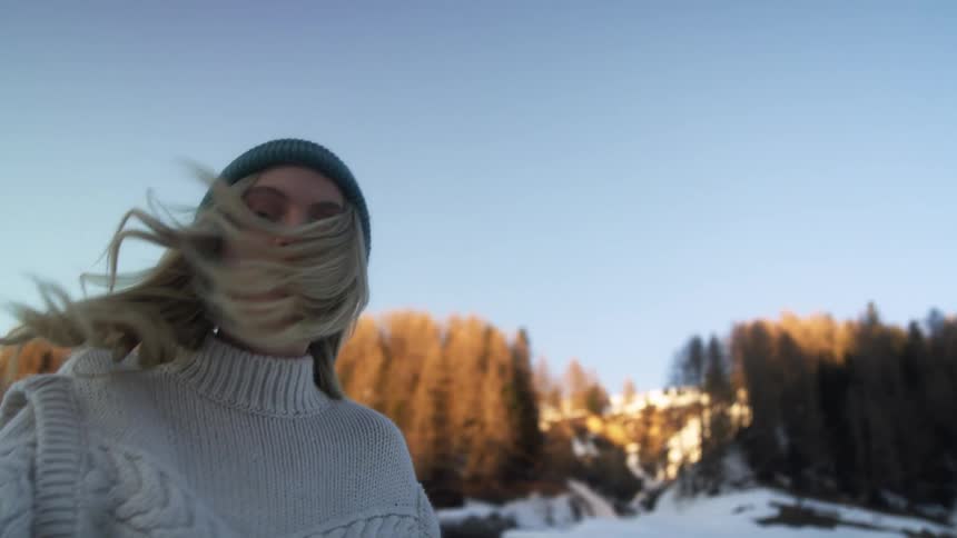 A woman with a sweater and hat with a snowy slope trees the sky and clouds in the background