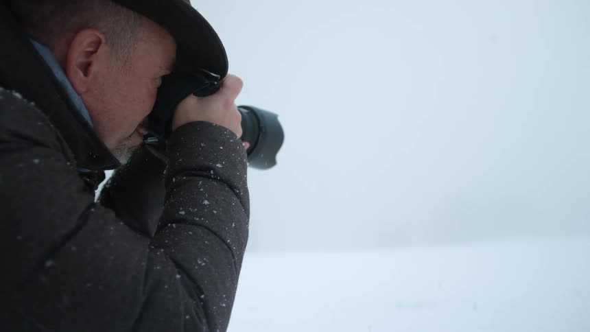 Photographer stands on snow covered ground taking picture as snow falls