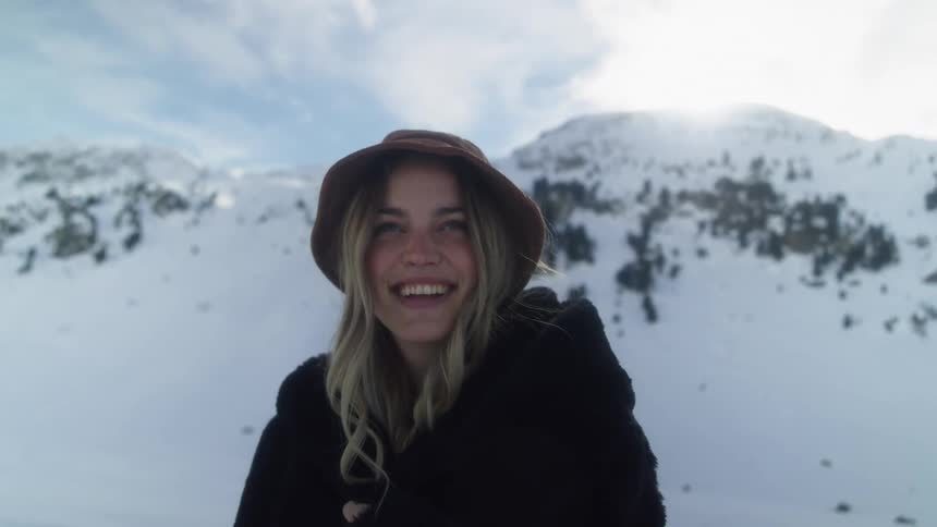 Woman wearing warm coat backed by snow covered mountains smiles
