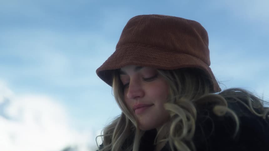 Woman stands with mountains on horizon rubbing hands then snuggling into coat