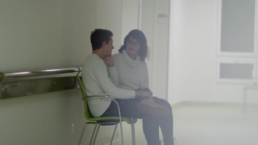 A woman listens to a man as they sit in chairs in a hallway
