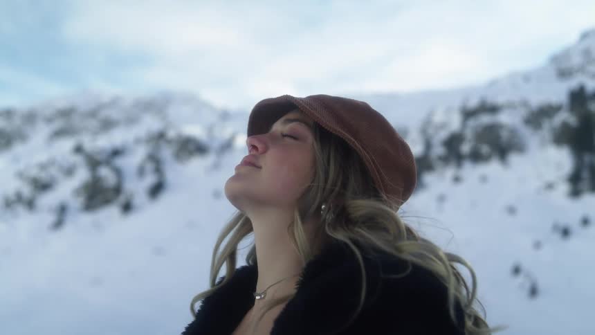 A young woman standing in front of a snow covered mountain looks up at the sky