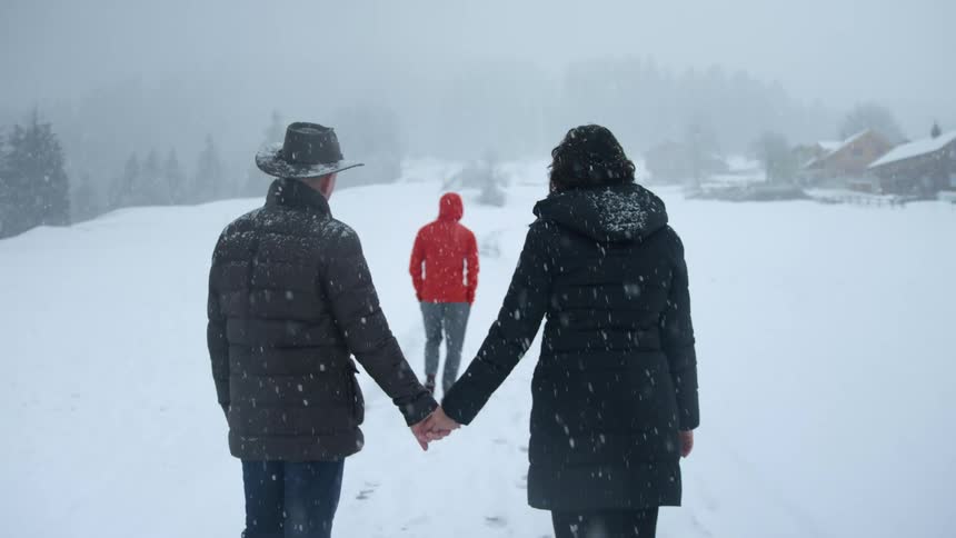 A man and woman holding hands outside in the snow while another person walks away from them