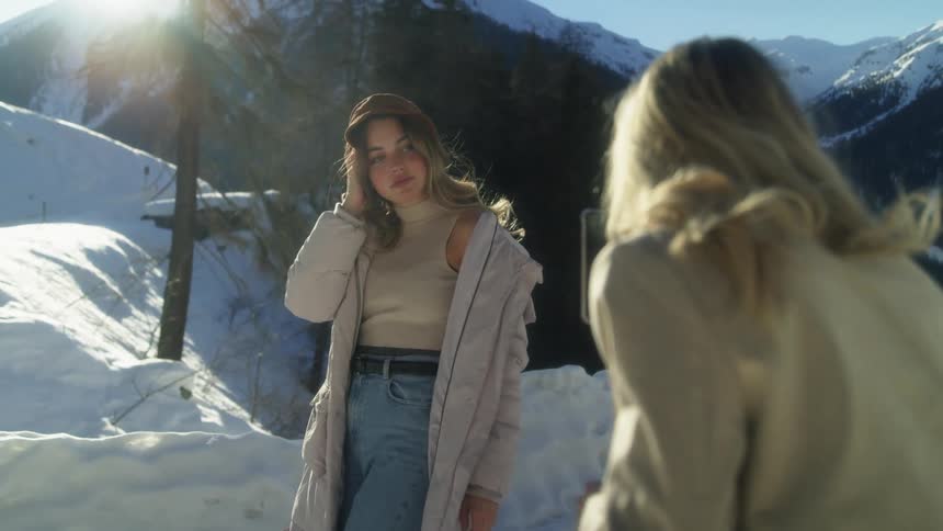 Woman takes pictures of a model with a smartphone on the snow in the mountains