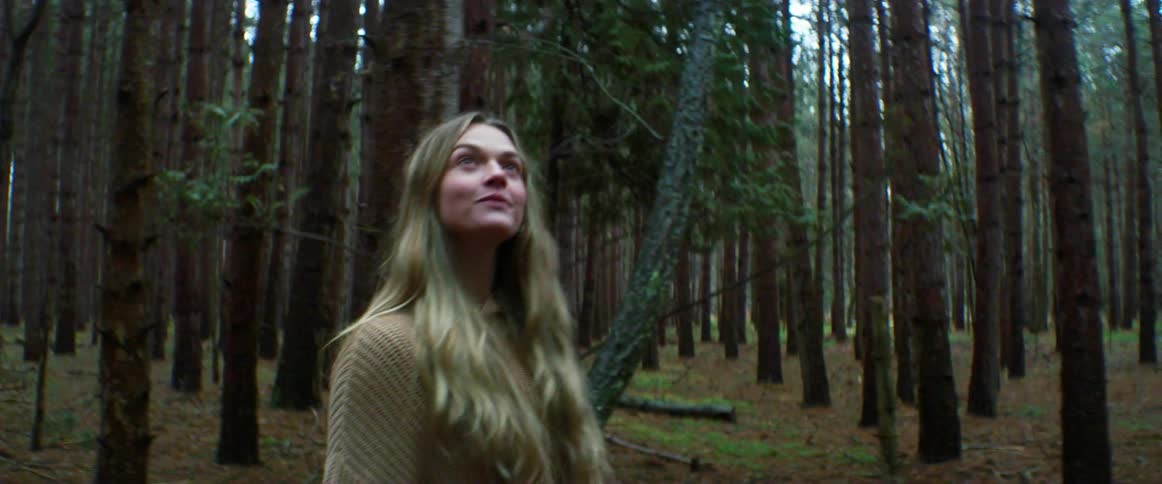 Blonde woman wearing sweater walks through forest smiling