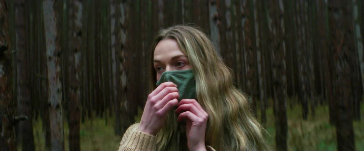 Blonde woman standing in the forest puts on a green cloth face mask