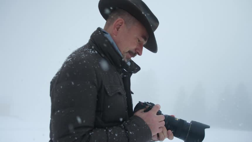 A male photographer takes a look at his camera settings while standing outside in the snow