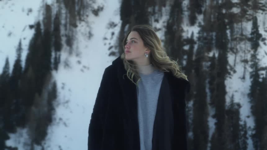 A woman walks through snowy woods with her black coat open
