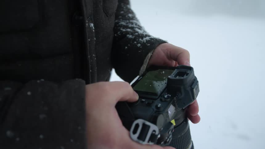 A photographer holding a camera outside while it snows in winter